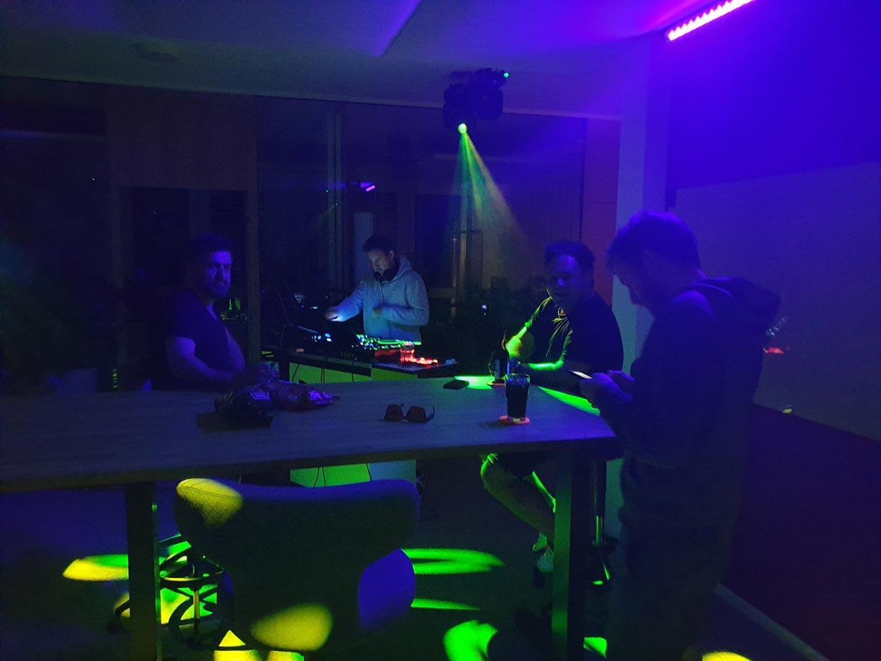 Foto von vier Personen, die im Büro eine Party mit Beleuchtung und DJ-Pult veranstalten.
